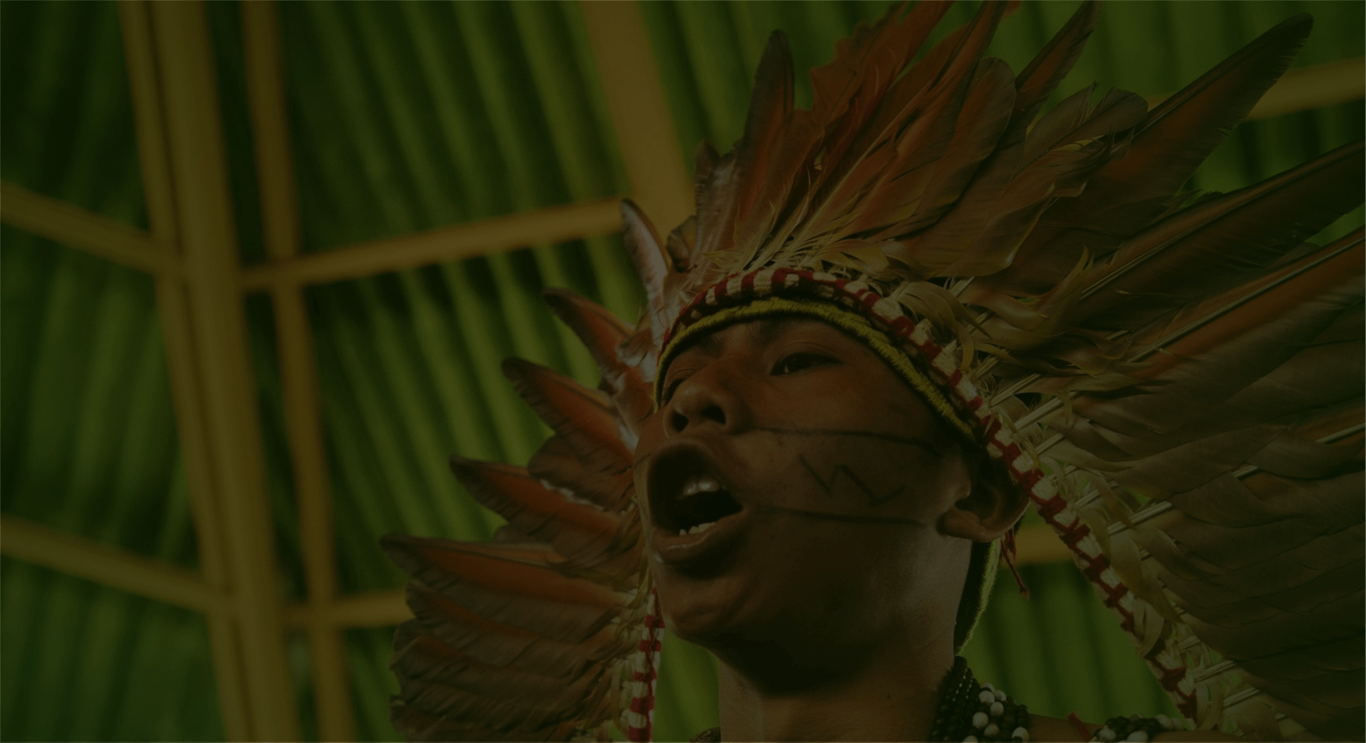 Homem indígena cantando com expressão de grito, expressando fortemente sua voz